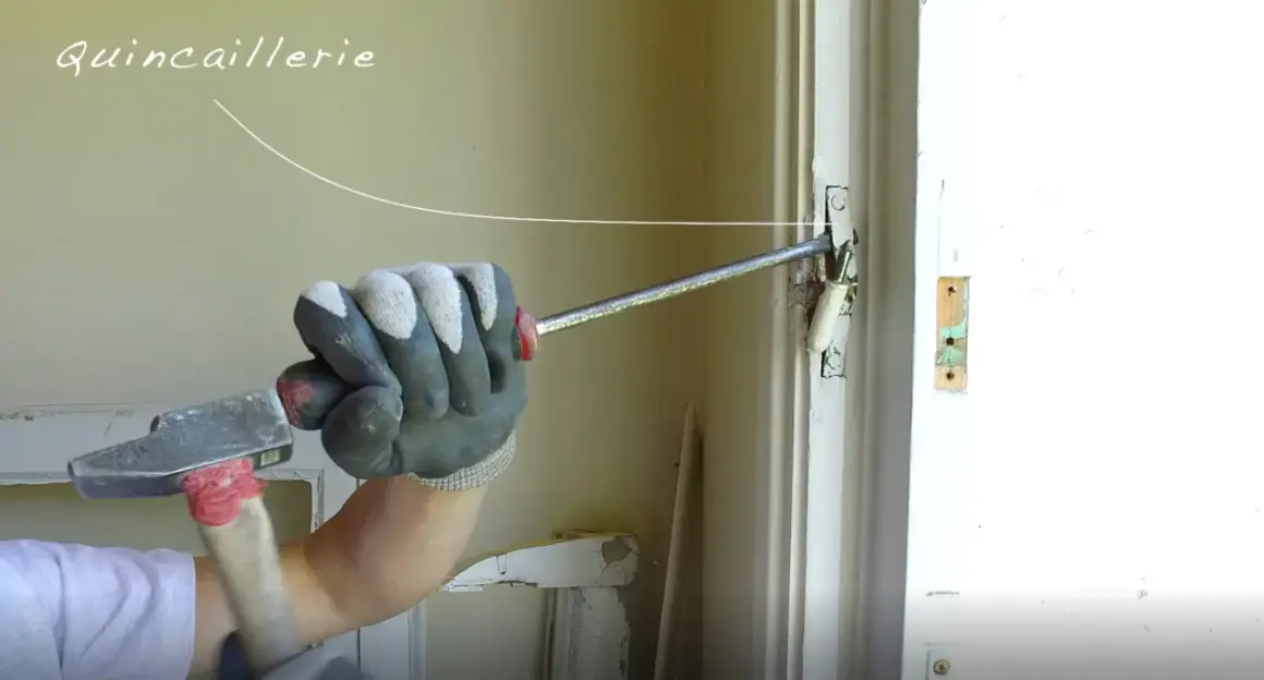 Main tenant utilise un marteau pour ajuster la quincaillerie d'une porte, travaillant sur une pose en feuillure.