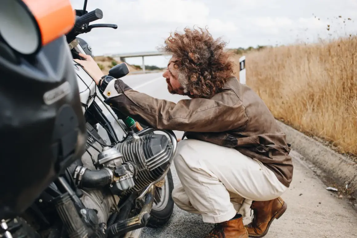 Hombre con pelo rizado revisa su moto 125, preguntándose cuanto aire lleva.