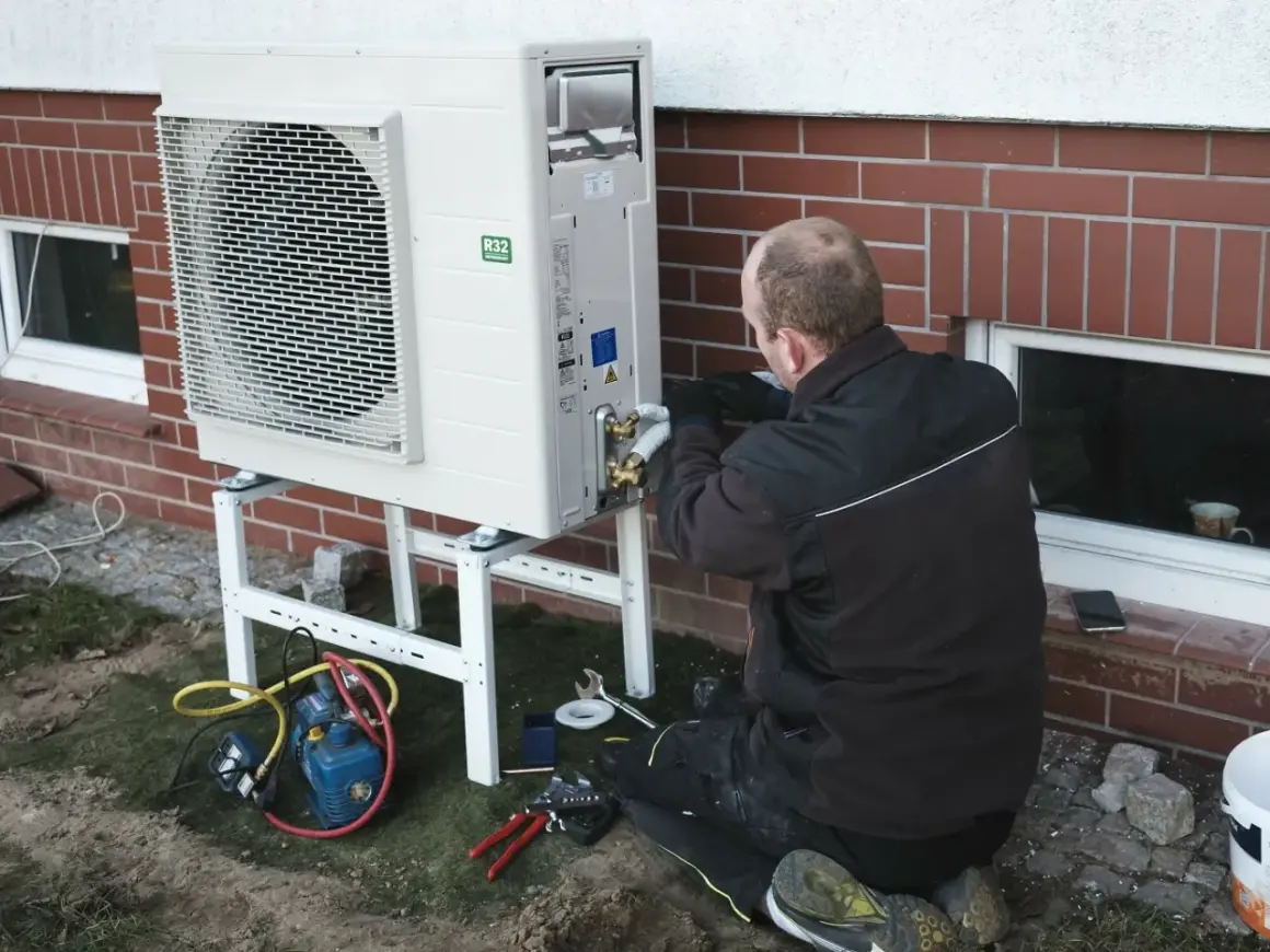 Instalator pracuje nad pompą ciepła, zapewniając jej ekonomiczne ustawienie. Widać narzędzia i sprzęt do montażu.