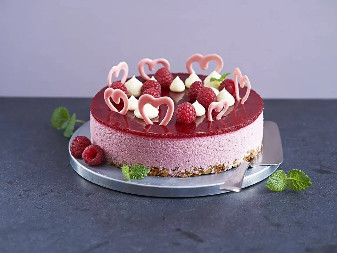 En vacker hallonmousse tårta med färska hallon och rosa hjärtdekorationer, perfekt för ett speciellt tillfälle.