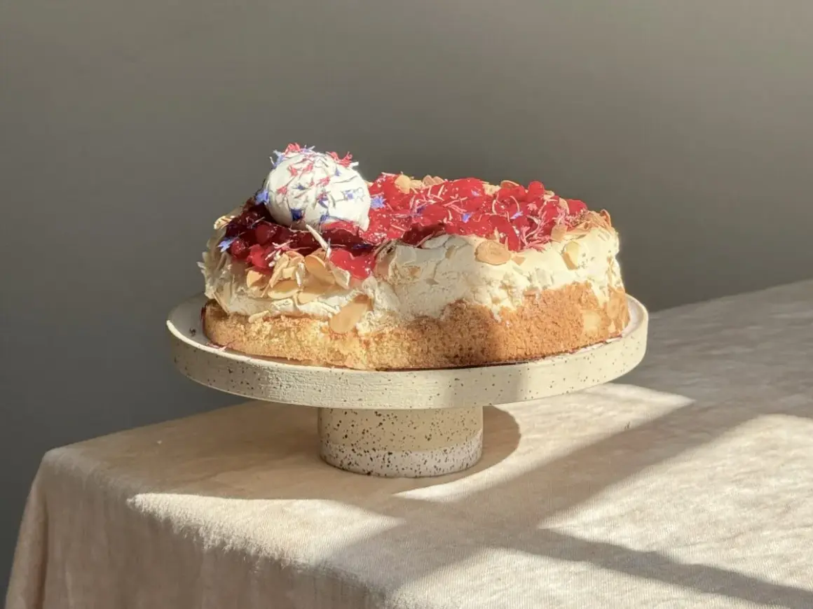 Eine köstliche Sommer Torte mit Baiserhaube, roten Beeren und Mandelsplittern, verziert mit essbaren Blüten.