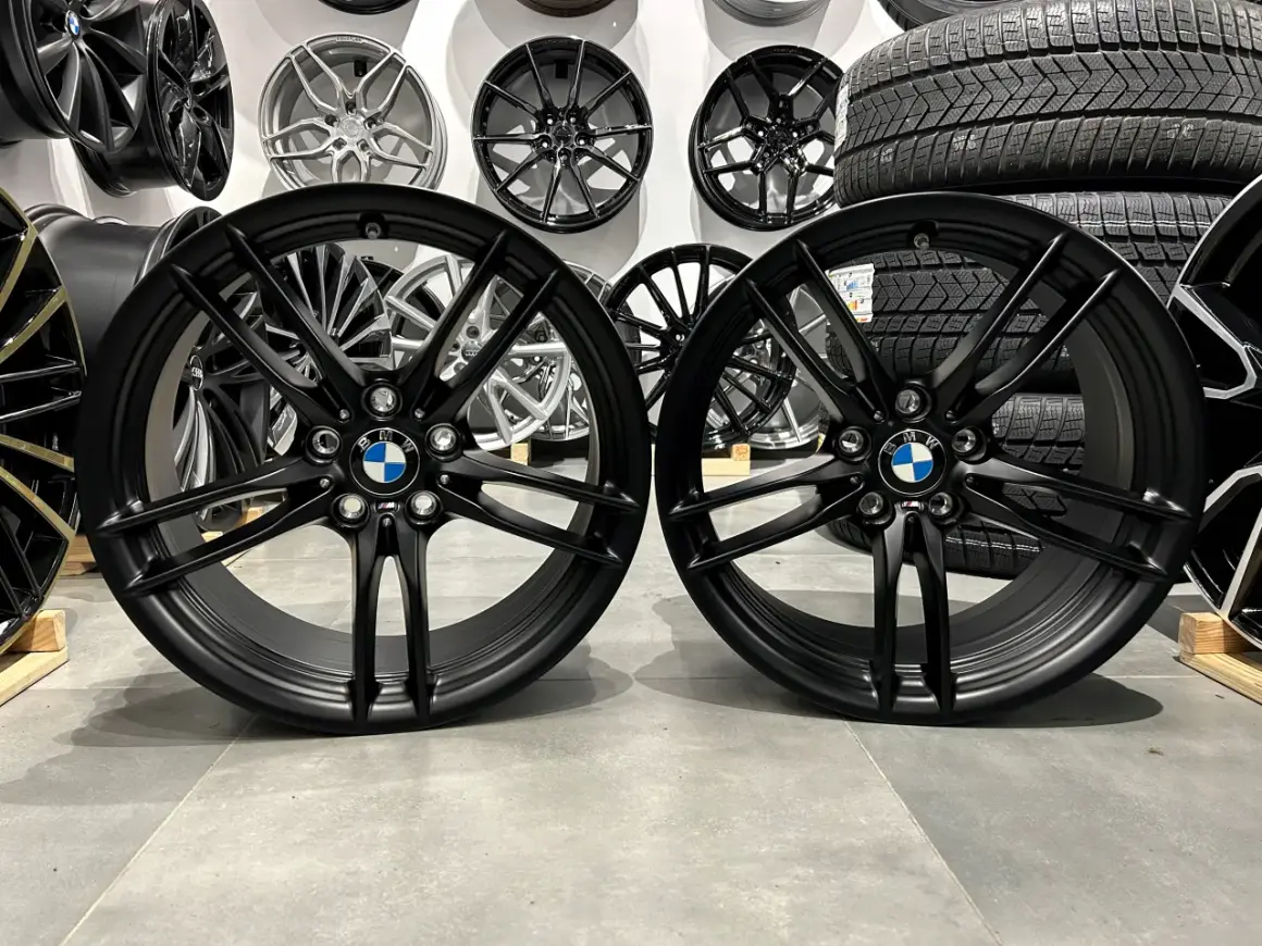 Dwa czarne felgi BMW z logo, idealne do tuningu. W tle inne felgi i opony.