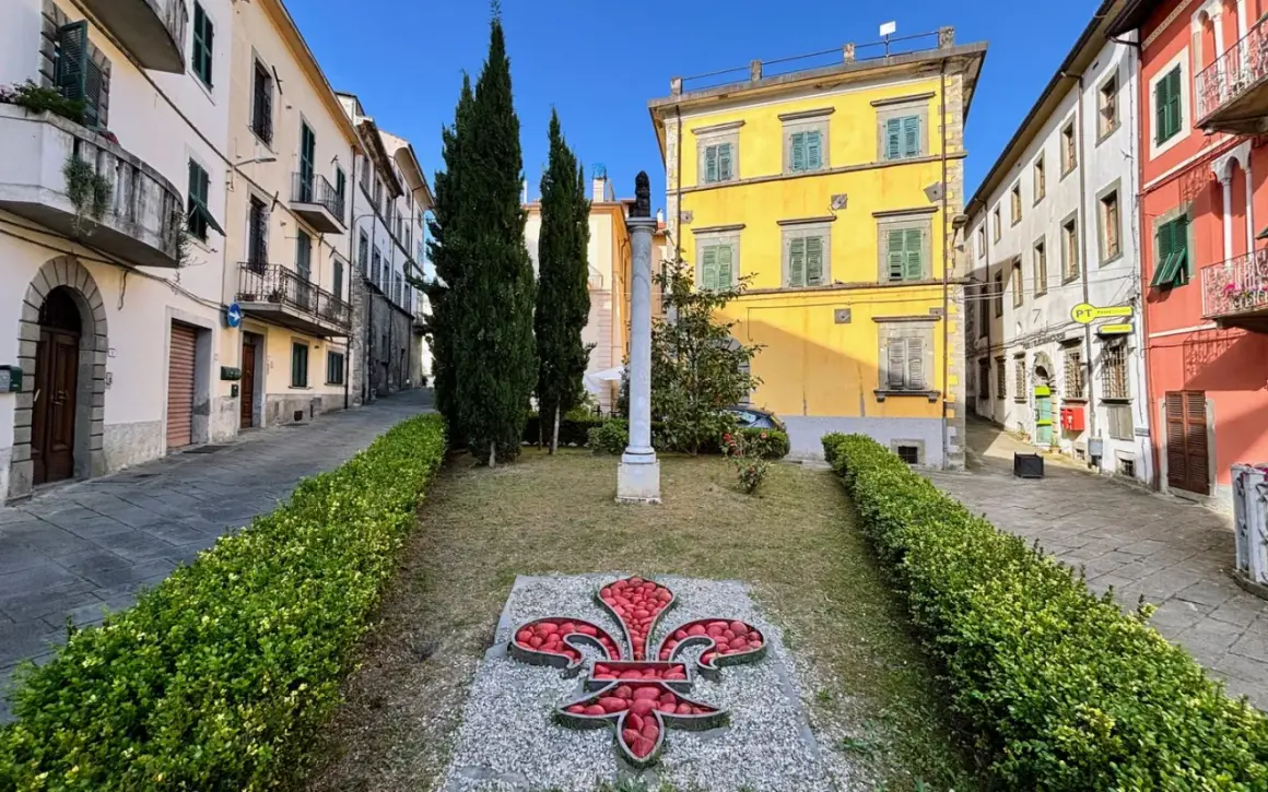Fivizzano cosa vedere: un'aiuola con un giglio rosso e un monumento in un vicolo con case colorate.