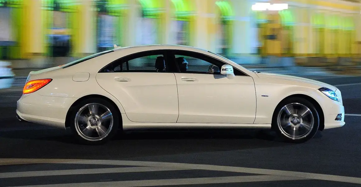 Biały Mercedes CLS 63 AMG mija nocą rozmyte światła miasta, jego sylwetka jest dynamiczna i elegancka.