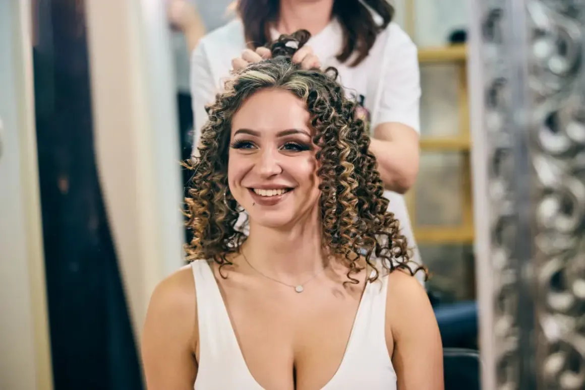 Une femme souriante se fait faire une permanente chez le coiffeur. Ses cheveux bouclés sont magnifiques.