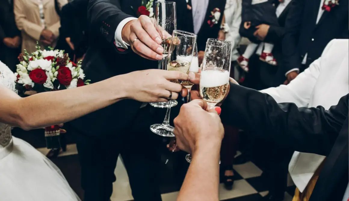 Para wznosi toast kieliszkami szampana. Zastanawiasz się, ile wódki na wesele? To zdjęcie nie odpowie, ale pokazuje radość!