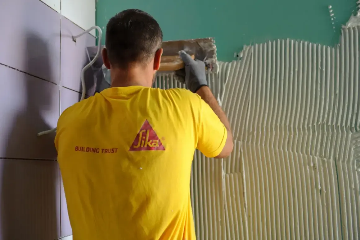 Operaio con maglia gialla Sika applica colla per incollare piastrelle su piastrelle parete.