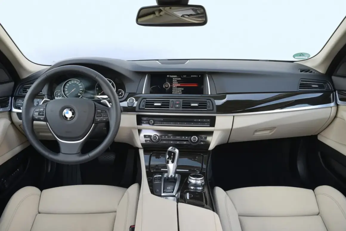 Wnętrze BMW F10 z jasną tapicerką, kierownicą, ekranem multimedialnym i panelem środkowym.