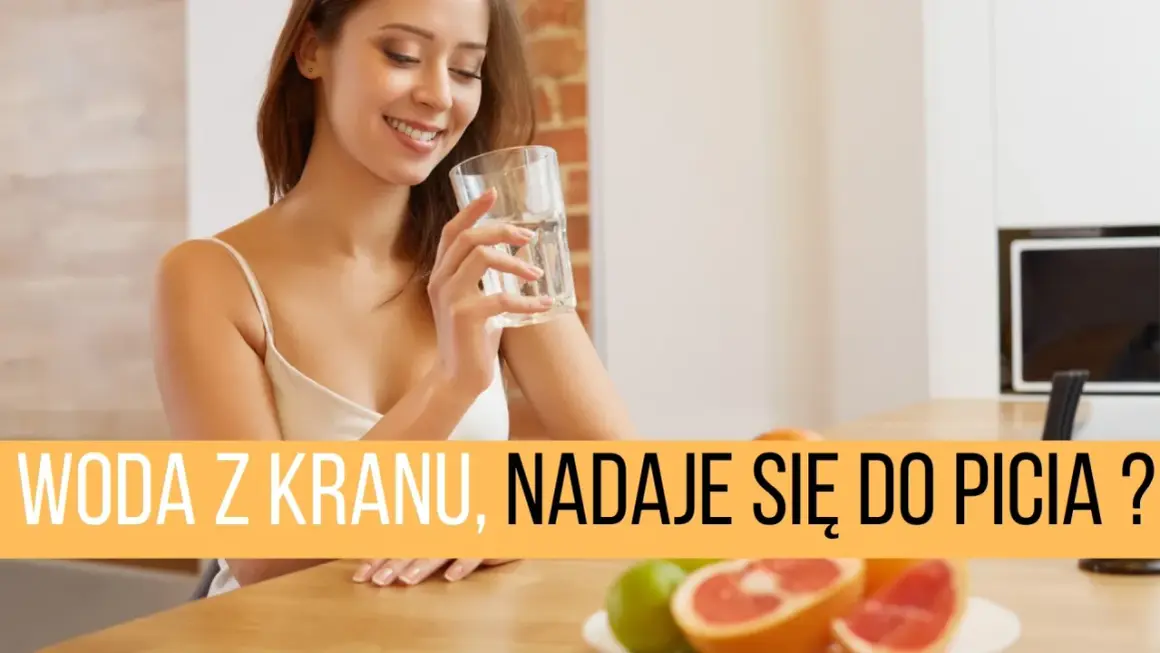 Uśmiechnięta kobieta pije wodę z kranu, zastanawiając się nad obecnością mikroorganizmów w wodzie pitnej.