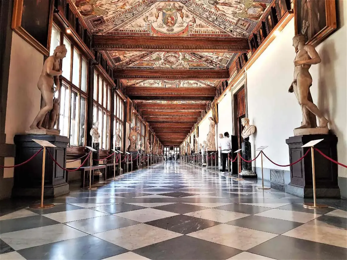Corridoio della **Gallerie des Offices Florence**, con statue classiche, soffitto affrescato e pavimento a scacchi.