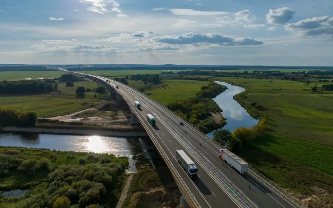 Most na Via Baltica przecina malowniczą dolinę rzeki, po której płyną ciężarówki.