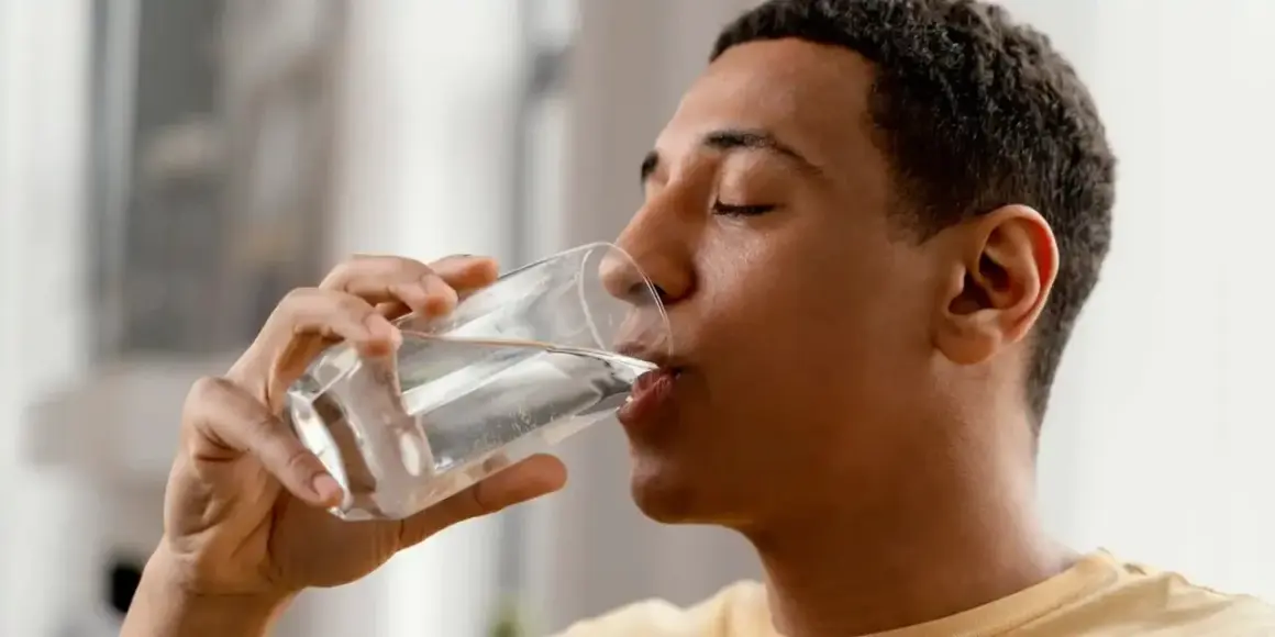 Un jeune homme boit un verre d'eau minérale magnésium, une boisson rafraîchissante et bénéfique.