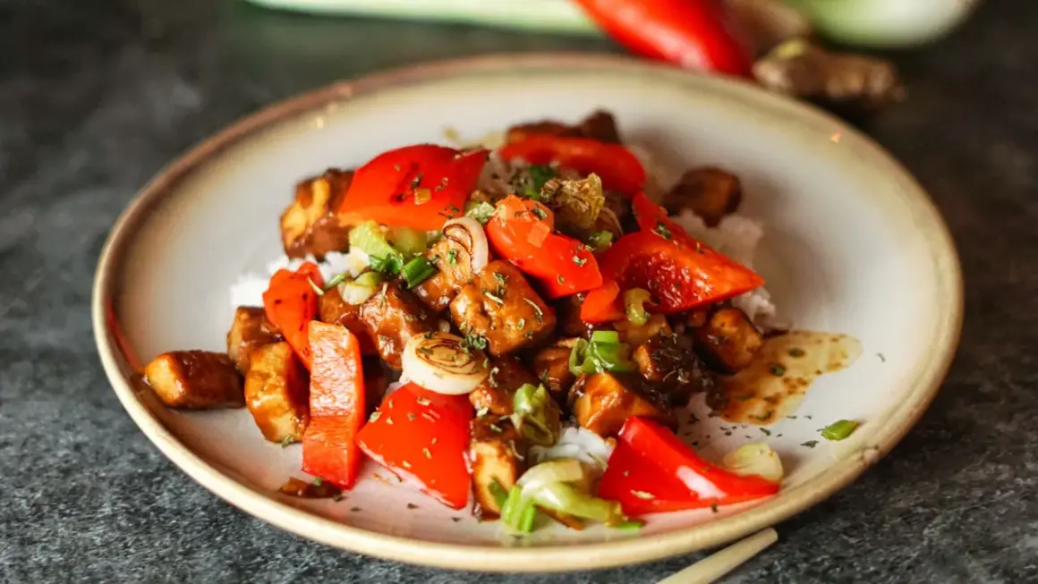 Leckeres, klebriges Tofu-Rezept mit Reis, Paprika und Frühlingszwiebeln, garniert mit Kräutern.