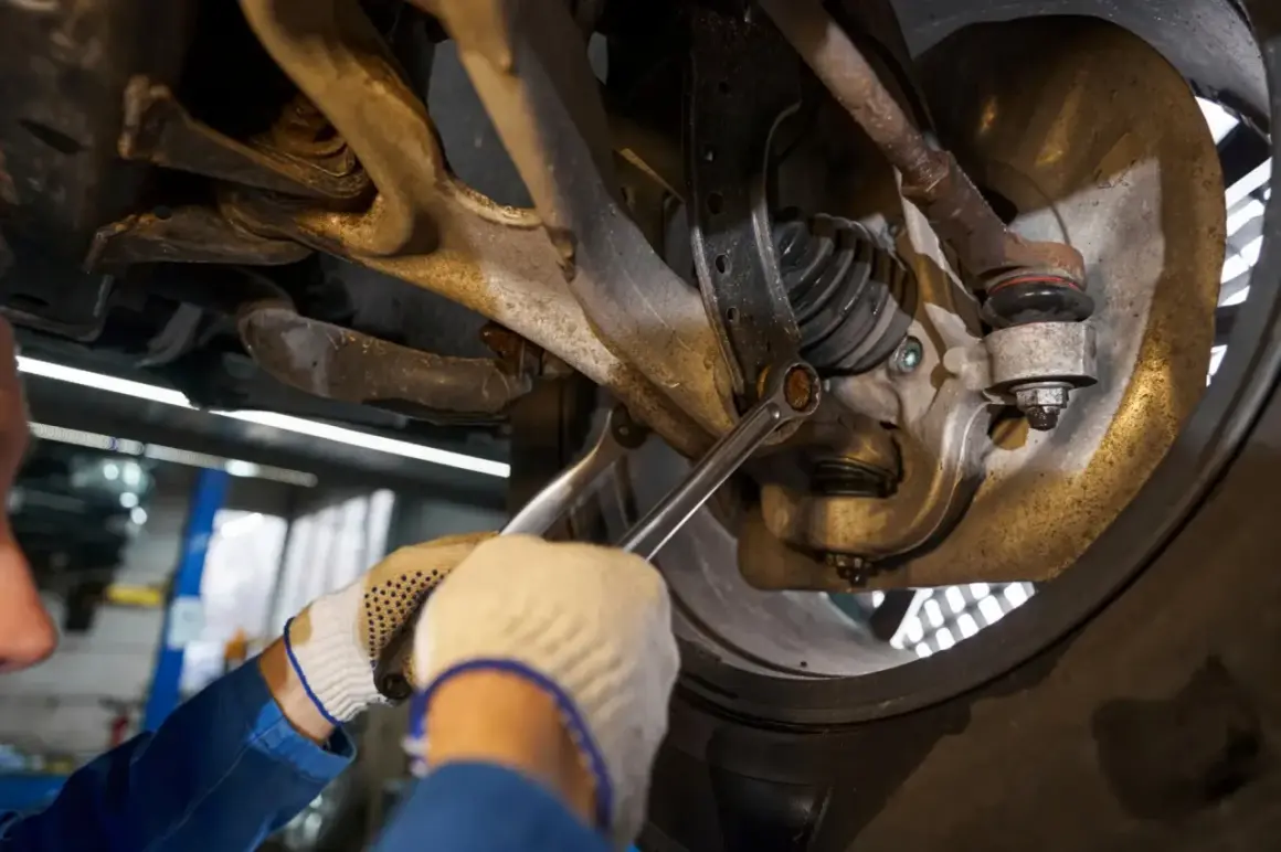 Mechanik dokręca śrubę w zawieszeniu samochodu kluczem.