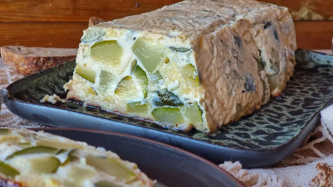 Pastel de calabacín casero, con trozos verdes visibles en una masa dorada, servido en plato oscuro.