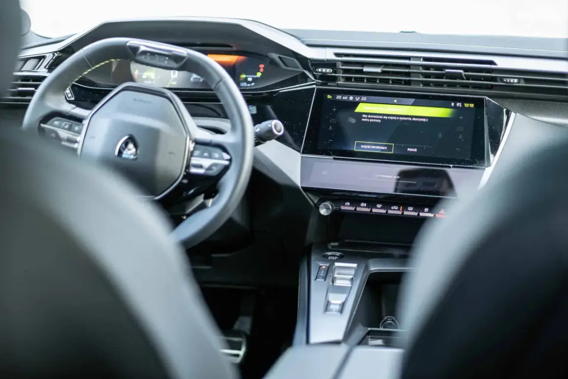 Nowoczesne wnętrze Peugeot 408 z cyfrowymi zegarami i ekranem dotykowym. Widoczny fragment kierownicy i konsoli środkowej.