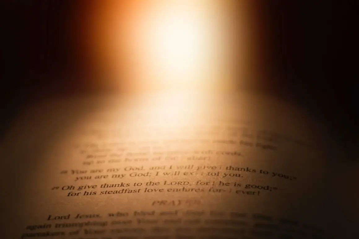 Otwarta Biblia, światło pada na tekst: "łaską jesteśmy zbawieni". Wersety Psalmów i modlitwa.