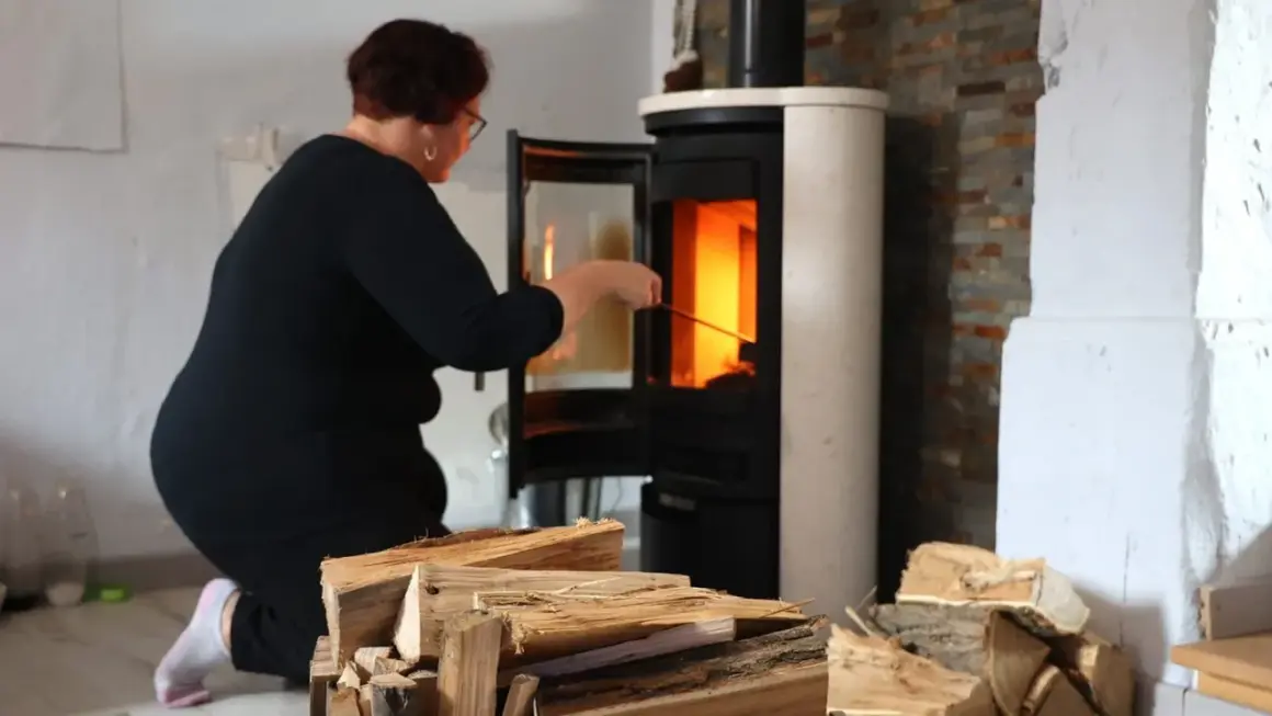 Frau kniet vor einem brennenden Kamin, um ihn zu reinigen. Holzscheite liegen bereit.