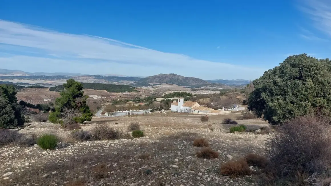 Paisaje de la sierra maria con una iglesia blanca y un campanario, rodeada de vegetación y montañas al fondo.