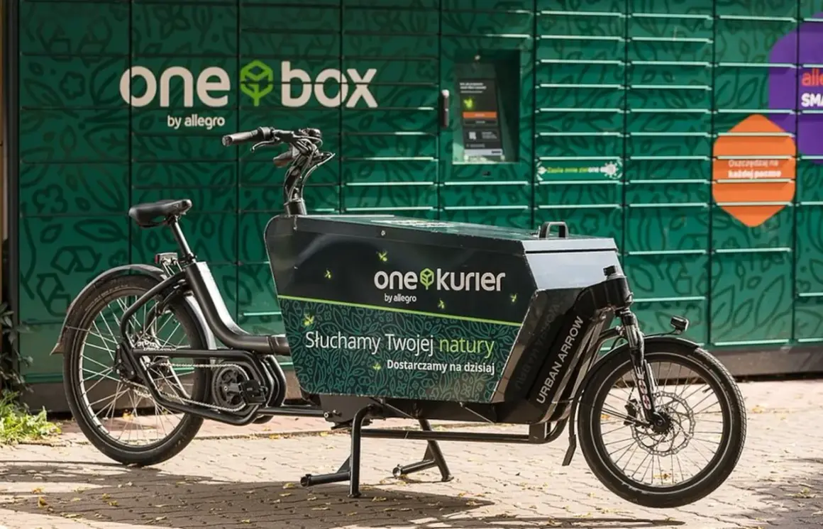 Rower cargo z napisem "one kurier by allegro" stoi przed zielonym paczkomatem "one box".