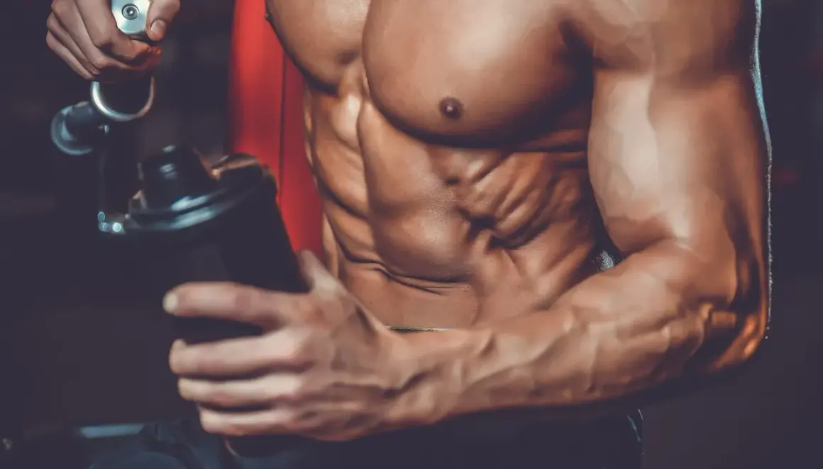 Atleta con addominali scolpiti prepara un frullato, mostrando a cosa servono le proteine in polvere palestra per la crescita muscolare.