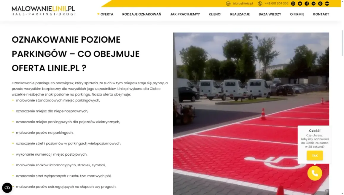 Malowanie oznaczenie miejsca dla niepełnosprawnych na czerwonym tle parkingu. W tle białe busy i drzewa.