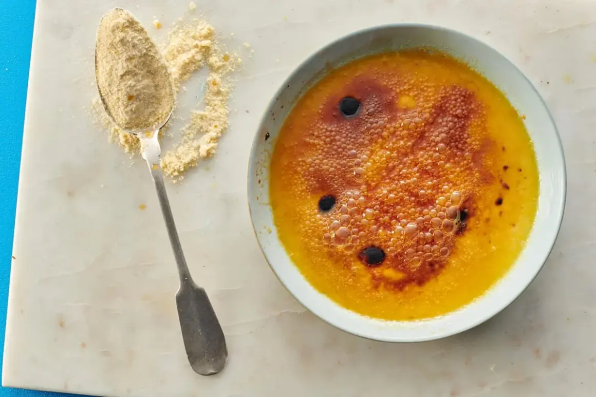 Ein Löffel mit feinem Puder liegt neben einer Schüssel mit karamellisiertem Creme Brulee.