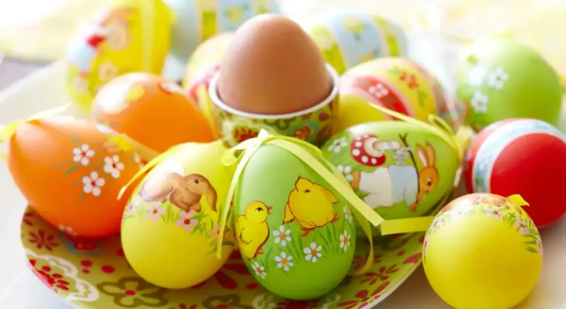 Un assortimento di colorate decorazioni uova di Pasqua con coniglietti, pulcini e fiori. Un uovo marrone è in un portauovo decorato.
