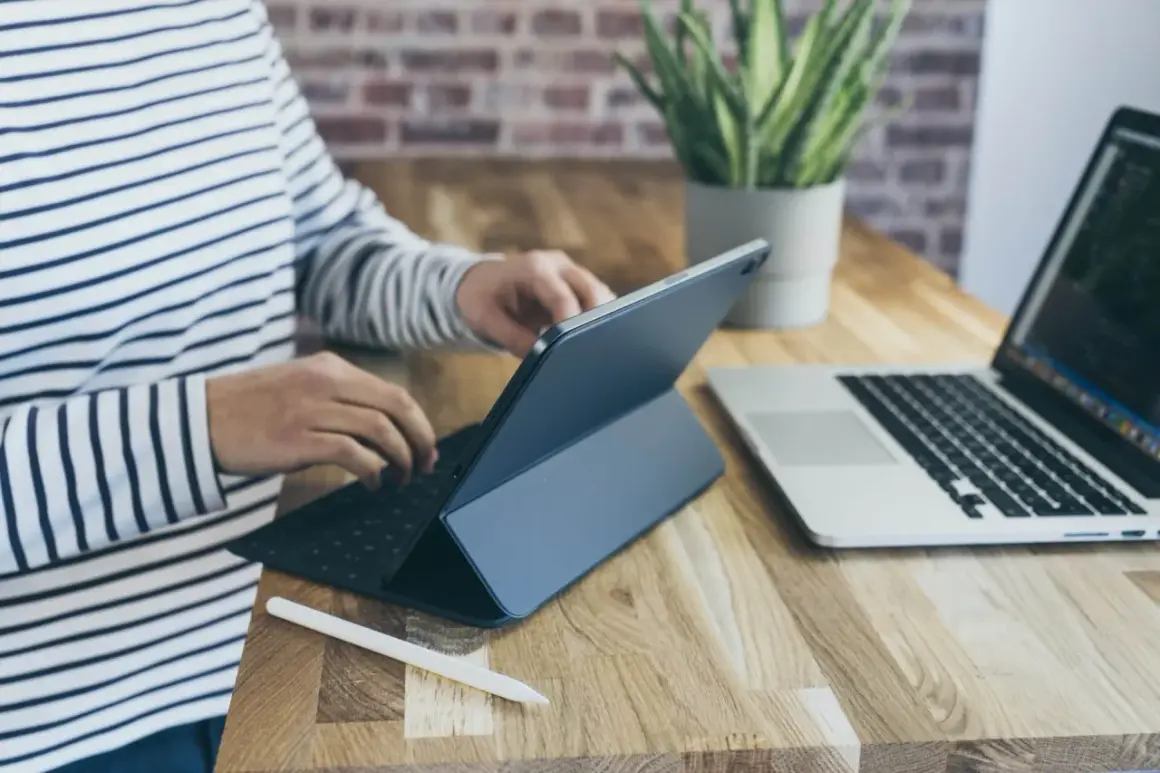 Osoba w paski pracuje na tablecie z klawiaturą, obok laptop. Może sprawdzać kursy walut w getin bank.
