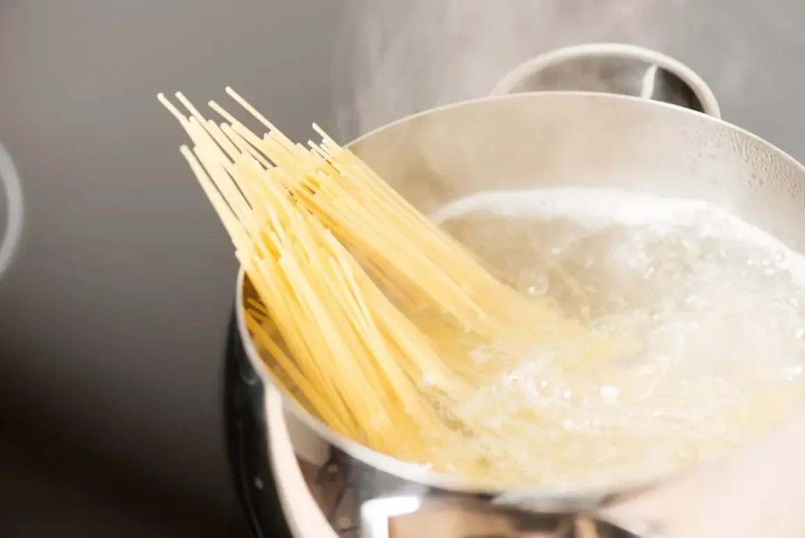 Kluska spaghetti zanurza się w gotującej wodzie. Czy wode na makaron sie soli? Tak, aby nadać jej smak.