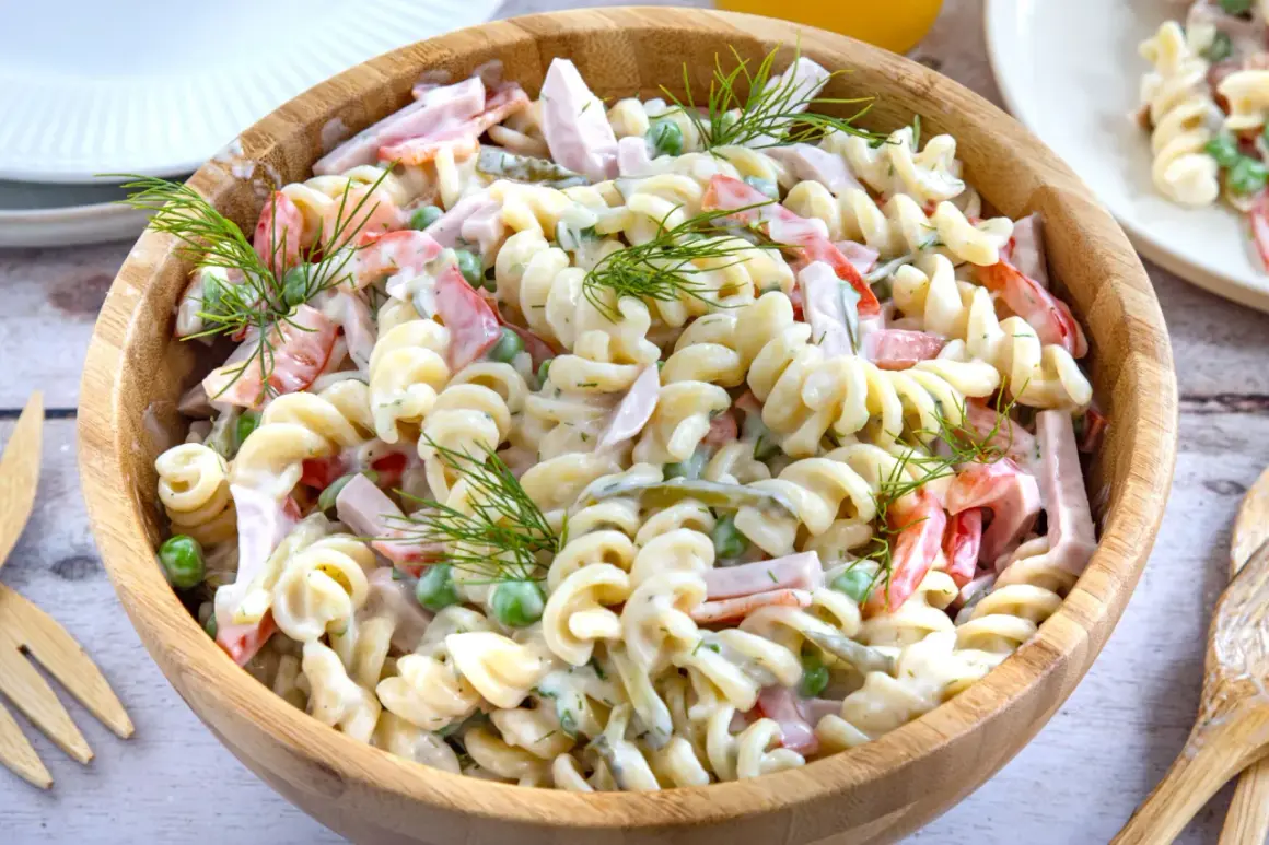 Ein cremiger Nudelsalat mit Schinken, Erbsen und Paprika, garniert mit Dill. Ein leckeres nudelsalat rezept für jede Gelegenheit.