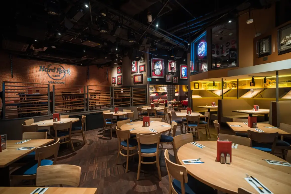 Wnętrze Hard Rock Cafe Warszawa. Drewniane stoły i krzesła, ściany ozdobione pamiątkami muzycznymi i neonem "Rock Radio".