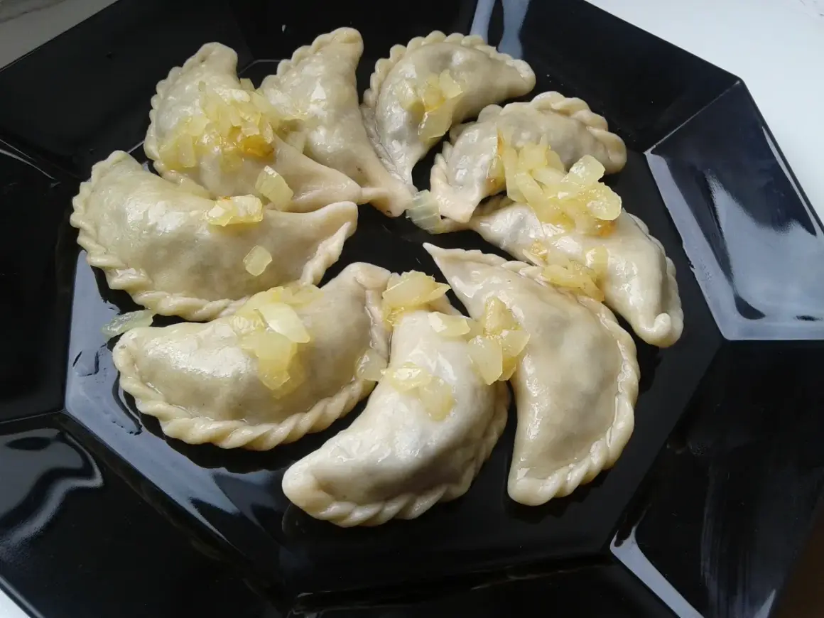 Pyszne pierogi z płuckami, polane skarmelizowaną cebulką, kuszą na czarnym talerzu.