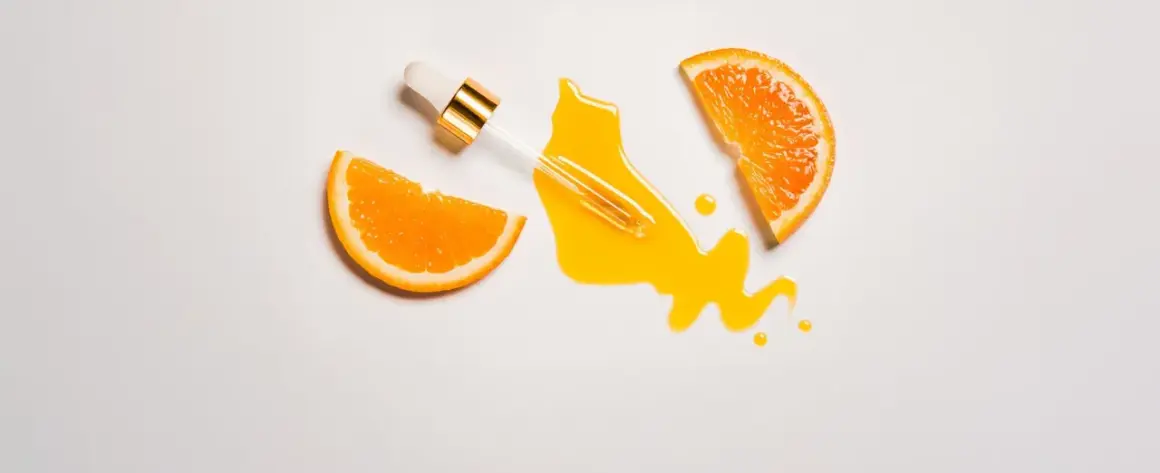 Ein Pipettenfläschchen tropft ein leuchtendes Serum neben Orangenscheiben. Vitamin C für das Gesicht, das für strahlende Haut sorgt.