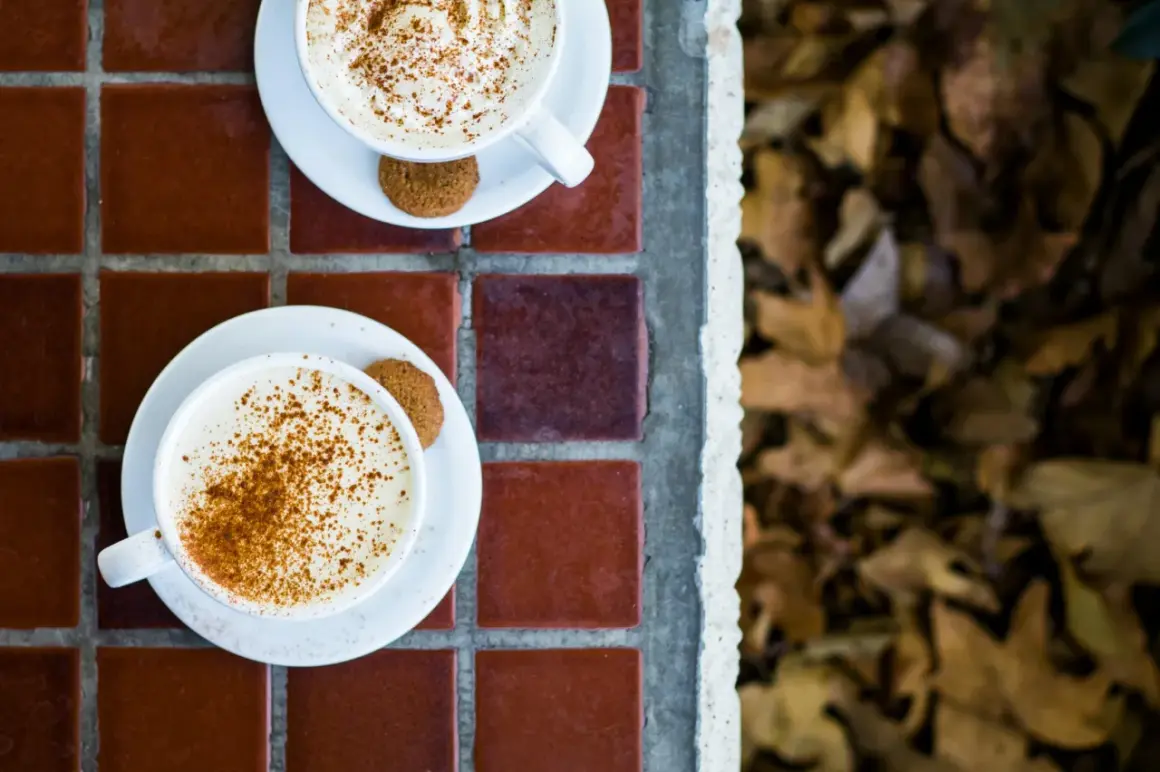 Två koppar med krämig pumpkin spice latte, toppade med kanel och en pepparkaka. Perfekt för ett mysigt pumpkin spice latte recept.