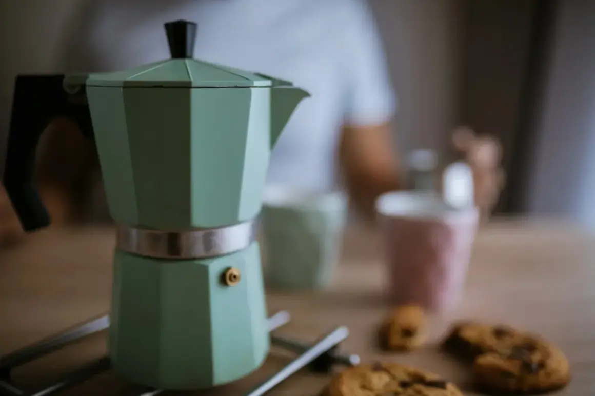 Moka verde pronta per il caffè, ma forse manca qualcosa per capire perche la moka non fa il caffe. Biscotti e tazze sullo sfondo.