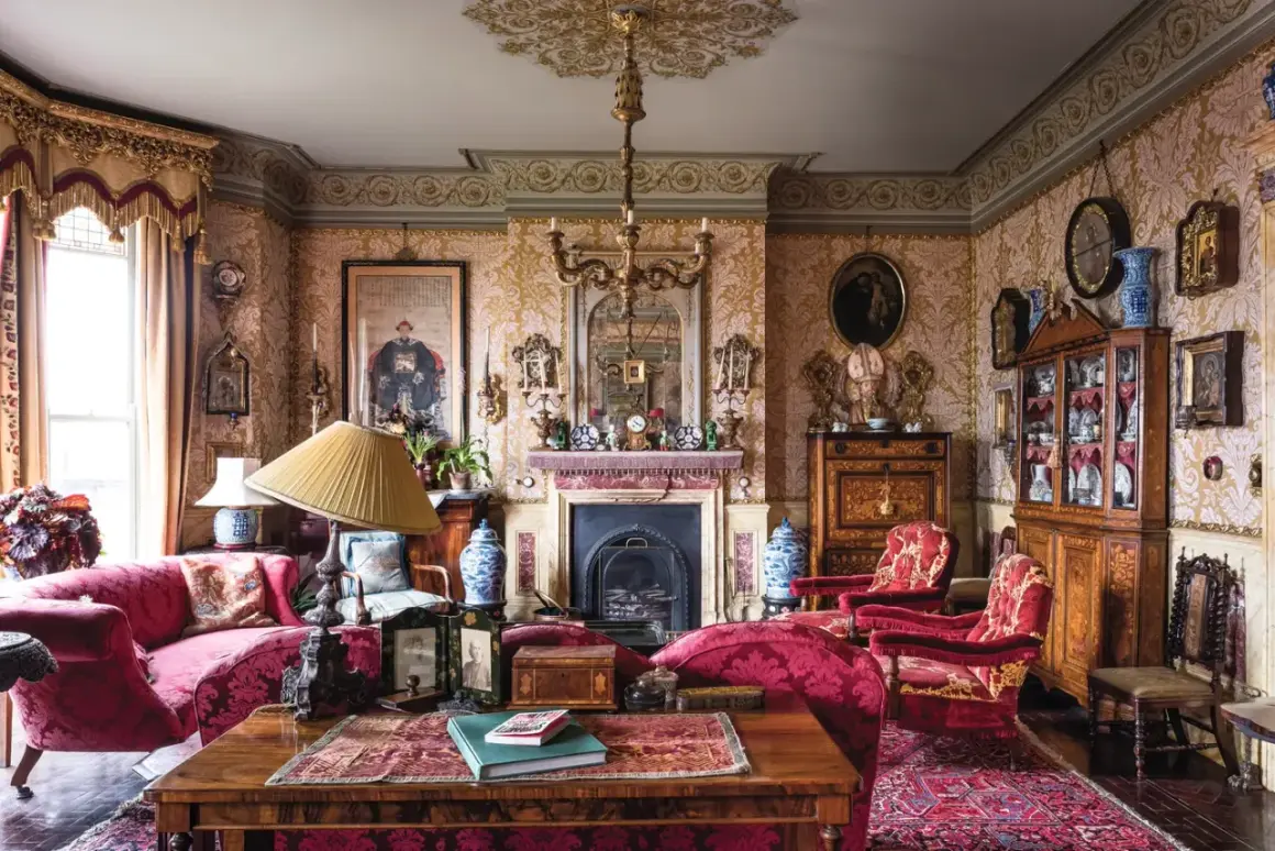 A lavish Victorian interior design with ornate wallpaper, plush red furniture, a fireplace, and antique decor.