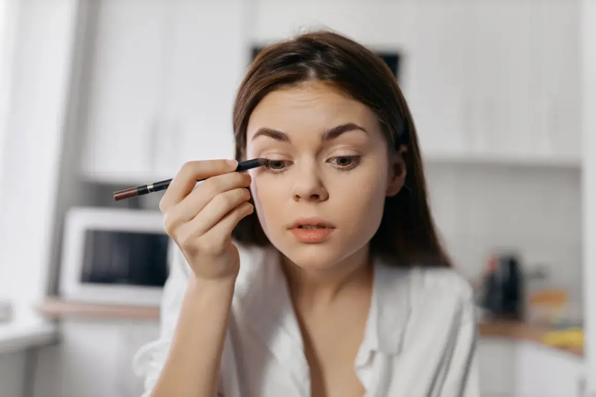 Dziewczyna wykonuje subtelny makijaż typu clean girl, precyzyjnie podkreślając oko kredką.