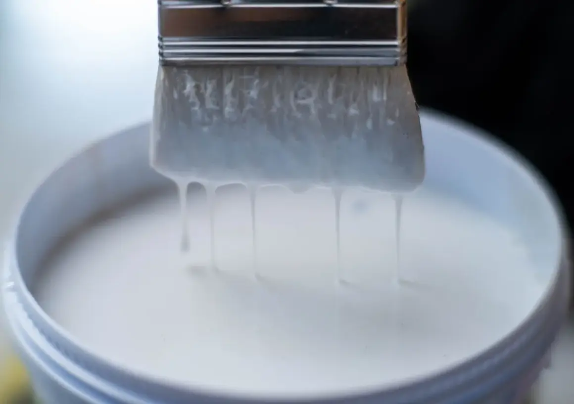 Pennello intriso di vernici all'acqua, gocciolanti in un secchio bianco.