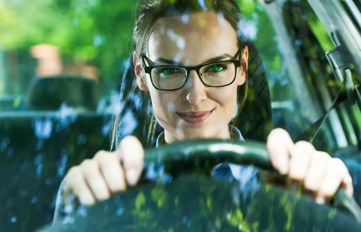 Frau mit Brille am Steuer, bereit zum Autofahren.