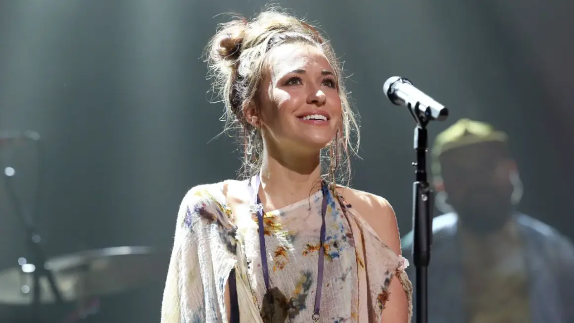 Lauren Daigle, mit hochgesteckten Haaren und einem bunten Kleid, singt auf der Bühne ins Mikrofon.