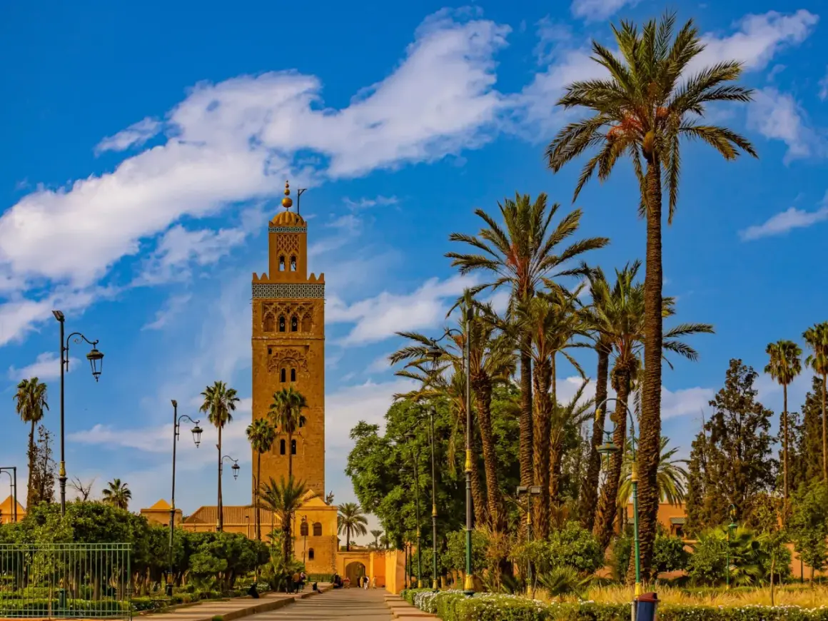 Torre Koutoubia, un lugar que ver en Marrakech, rodeada de palmeras y bajo un cielo azul con nubes.