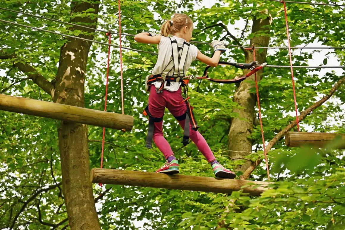Ein Mädchen balanciert auf einem Baumstamm in einem Kletterpark. Ein spannendes Abenteuer für die **Herbstferien 2026**!