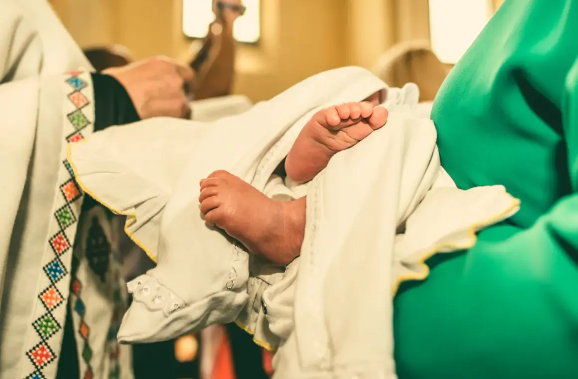 Les petits pieds d'un bébé, enveloppés dans un linge blanc orné, lors d'un baptême catholique.