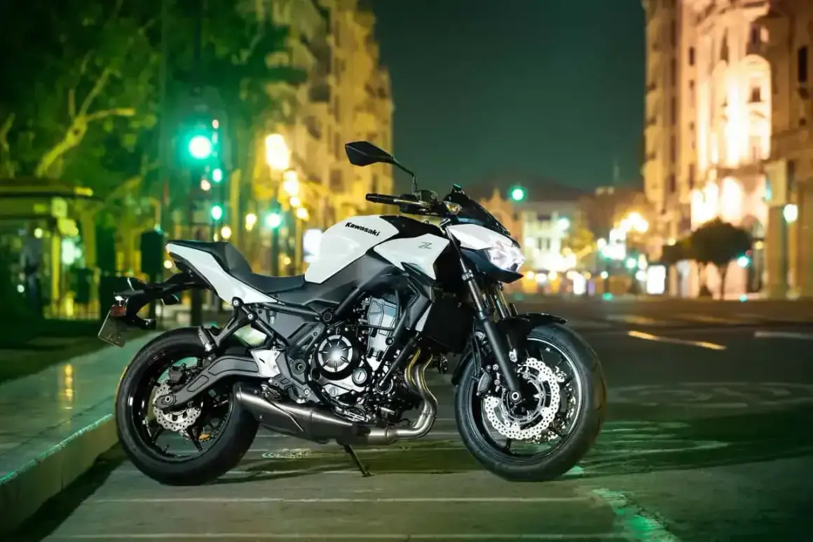 Kawasaki z650 cv blanca y negra, aparcada en una calle urbana de noche, con luces de edificios y semáforos de fondo.