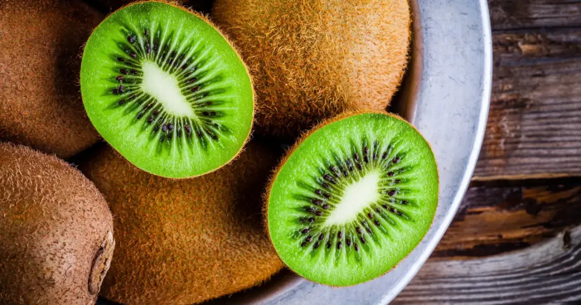 Kiwifruit w misce, przekrojone na pół, ukazujące zielony miąższ z czarnymi pestkami.
