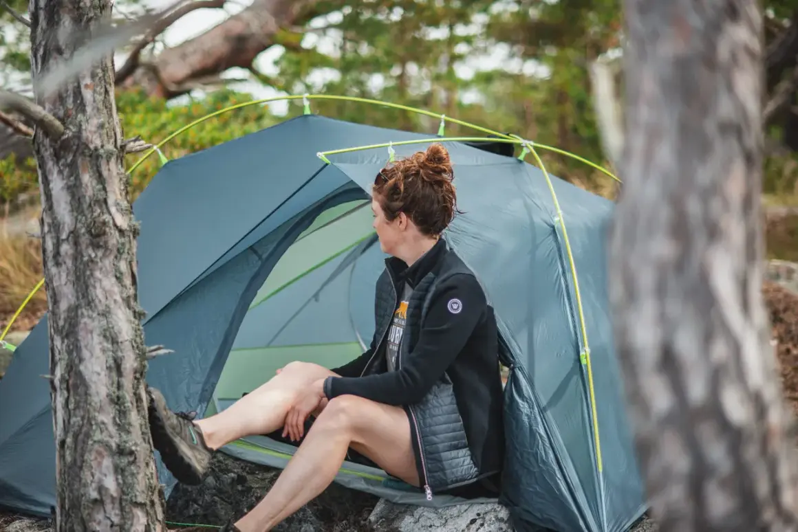Kvinna vilar vid sitt tält, redo för camping i naturen.