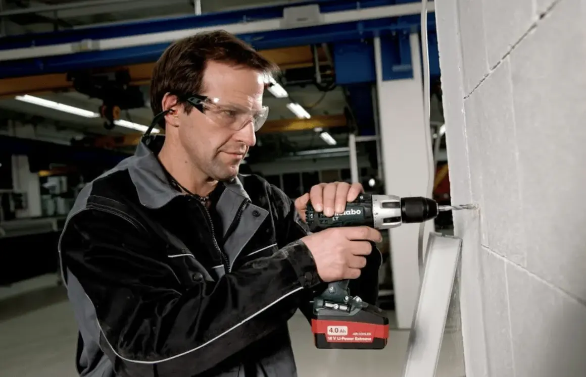 Un ouvrier utilise une perceuse sans fil Metabo, dont l'origine est allemande, pour percer un mur en parpaings.