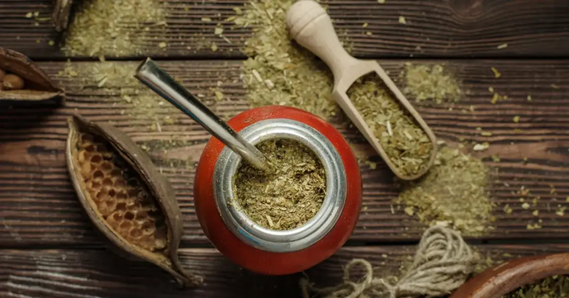 Czerwone naczynie z bombillą, drewniana łopatka z suszem i strąki – wszystko to sugeruje bogactwo yerba mate właściwości.