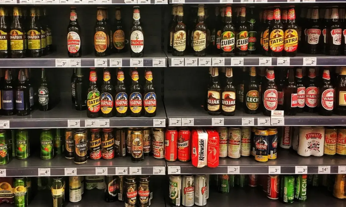 Półki sklepowe uginają się pod ciężarem piwa na półce. Butelki i puszki różnych marek tworzą kolorowy krajobraz.